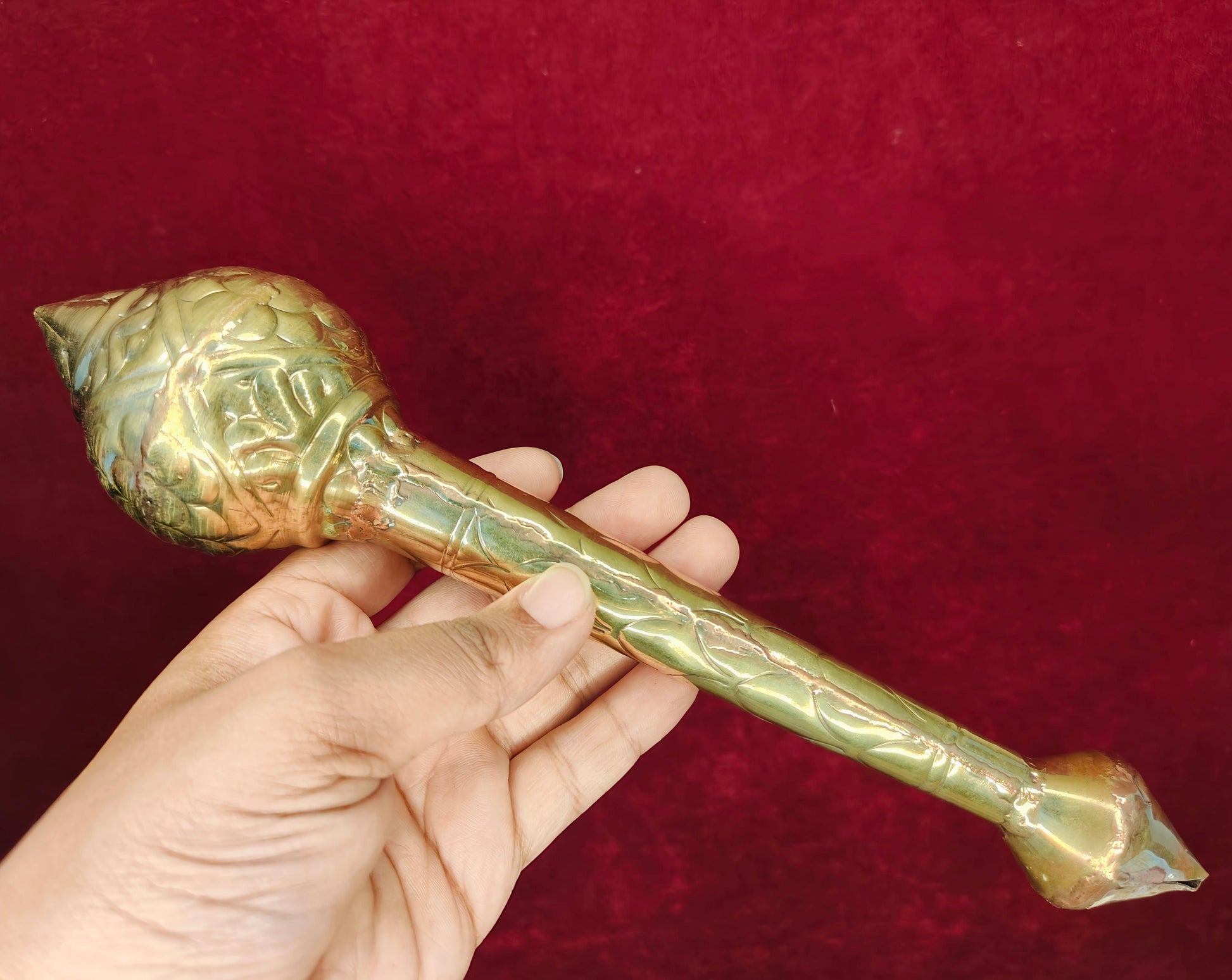 Gold-colored peetal decorative gada held in a hand against a red background
