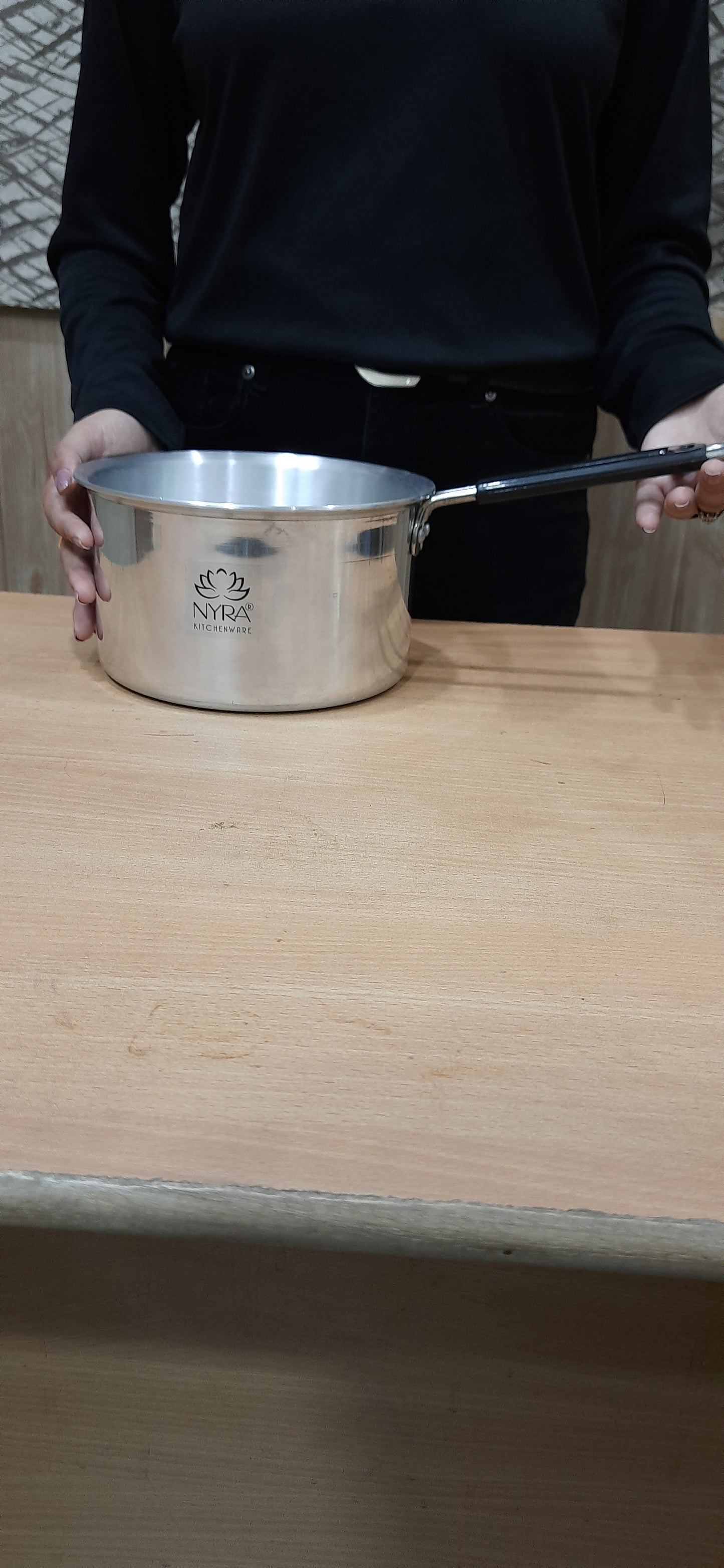 Person holding a metallic container with a lid on a wooden surface