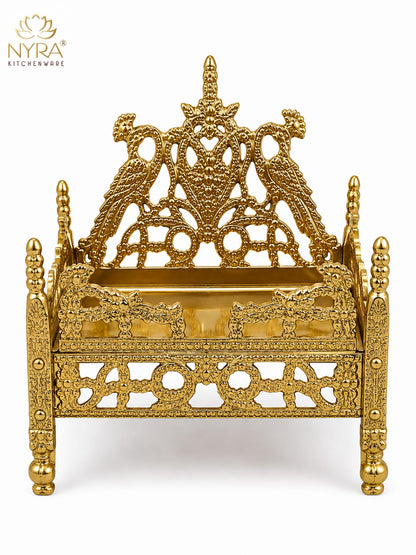 An ornate gold-plated brass miniature throne or palanquin with intricate filigree cutouts, decorative pillars, and a detailed crest on the backrest, shown on a white background with the NYRA Kitchenware logo in the top left corner.