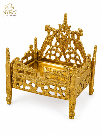 An ornate gold-plated brass miniature bed with intricate filigree cutouts and a reflective tray, shown on a white background with the NYRA Kitchenware logo in the top left corner.