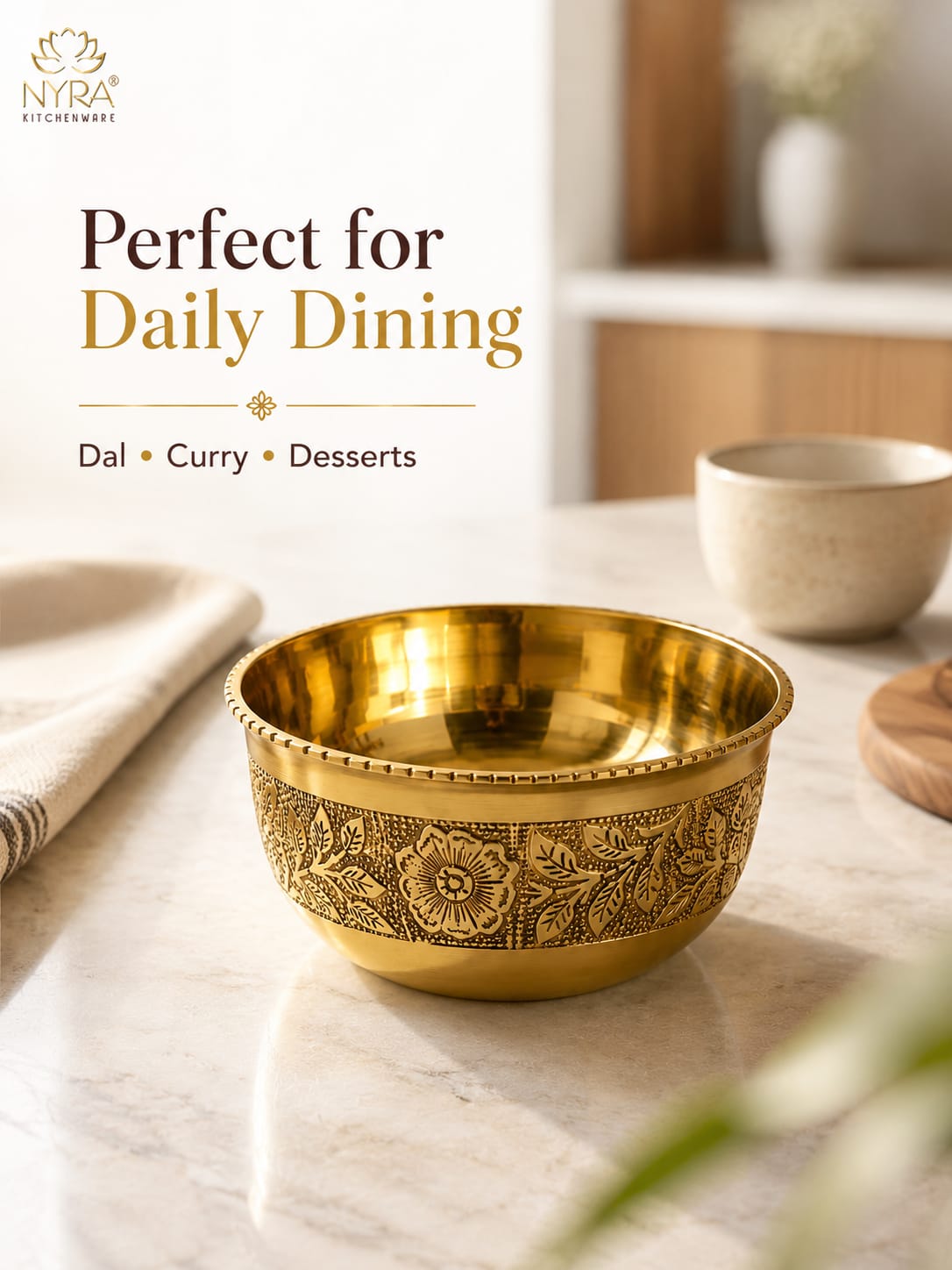 A shiny gold-toned metal bowl with embossed floral detailing around the lower half, placed on a light marble surface in a softly blurred kitchen setting. Text on the left reads 'Perfect for Daily Dining' with 'Nyra Kitchenware' at the top.