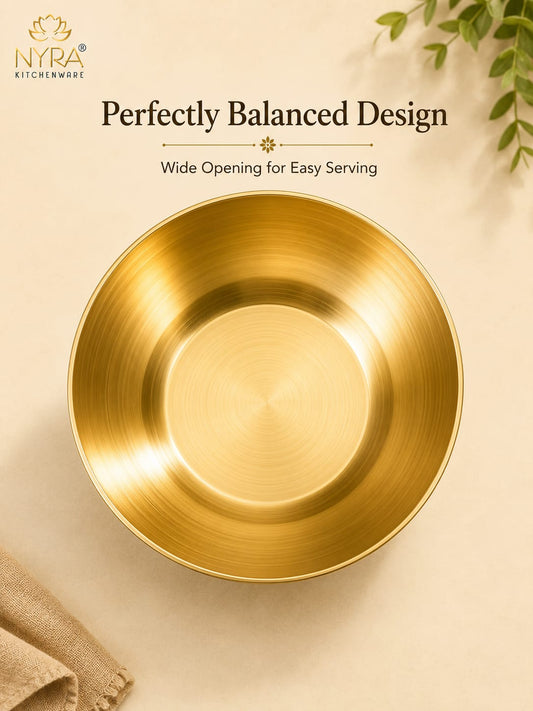 A brushed gold NYRA kitchenware bowl shown from above on a warm beige background with decorative text and small plant/napkin props. The image highlights the bowl's wide, balanced opening and clean metallic finish.