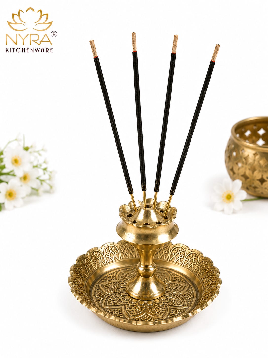 A brass incense holder with five black incense sticks, shown on a white background with decorative flowers and a brand logo for NYRA Kitchenware.