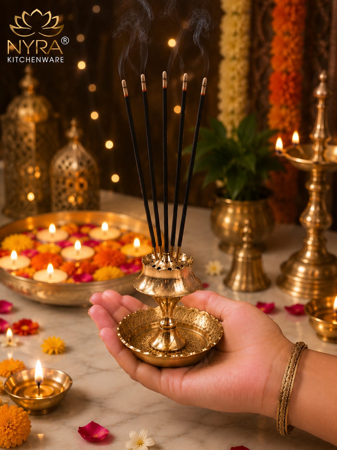 A hand holds a brass incense holder with several smoking incense sticks, set against a festive background with lit candles, marigolds, and decorative brass vessels. The NYRA Kitchenware logo is visible in the top left corner.