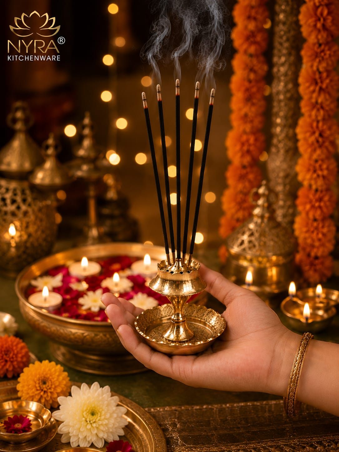 A hand holds a brass incense holder with several smoking incense sticks, set against a warm, festive background with marigold garlands, floating candles, and NYRA Kitchenware branding.
