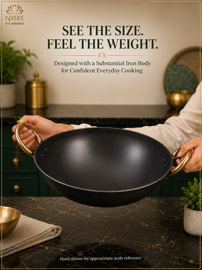 A person holds a large black cast-iron wok with brass handles over a kitchen counter, with promotional text above reading 'SEE THE SIZE. FEEL THE WEIGHT.
