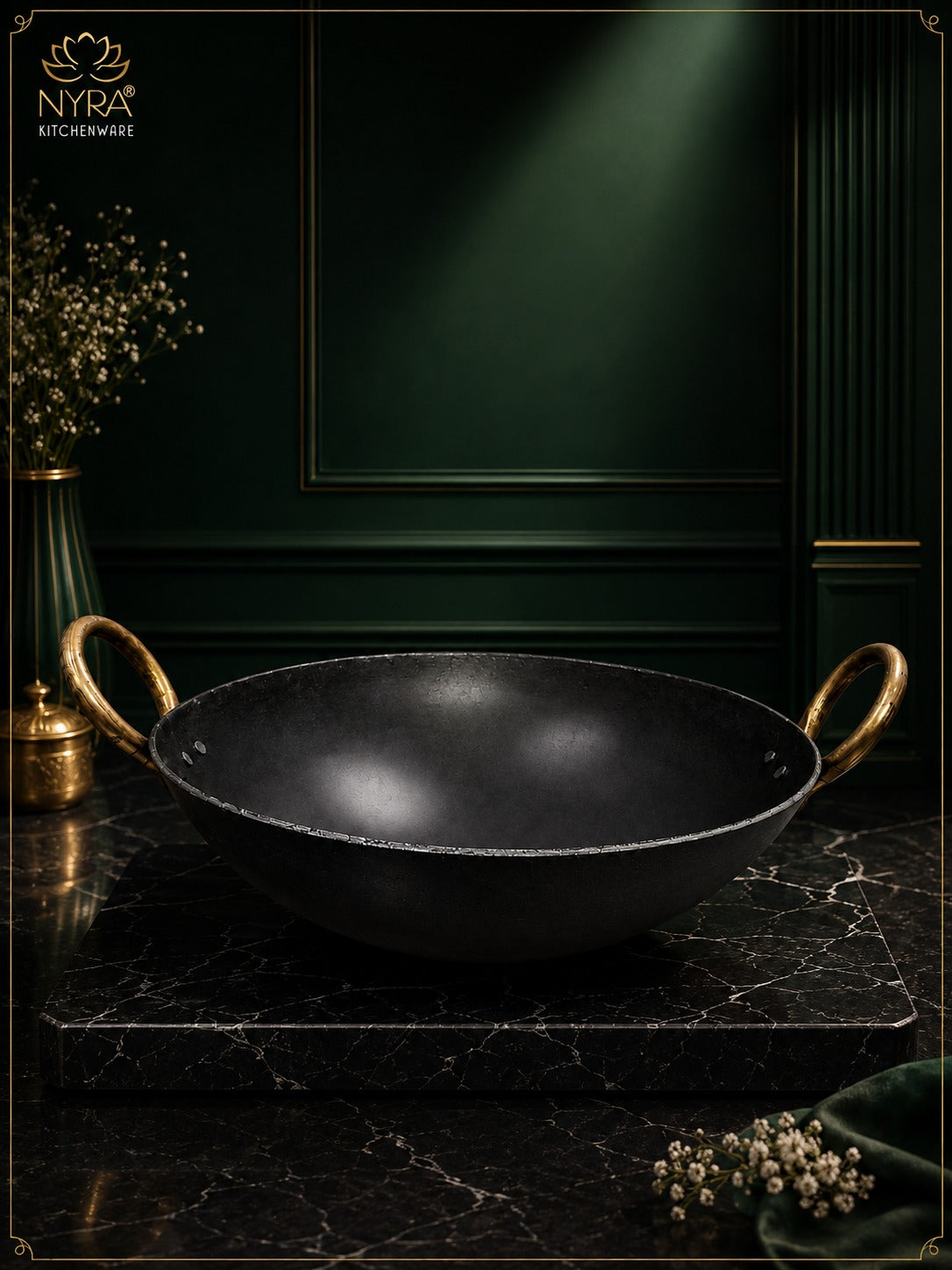 A black cast iron kadhai wok with gold-toned loop handles, displayed on a dark marble slab against a dark green paneled background. The brand logo 'NYRA KITCHENWARE' is visible in the top left corner.