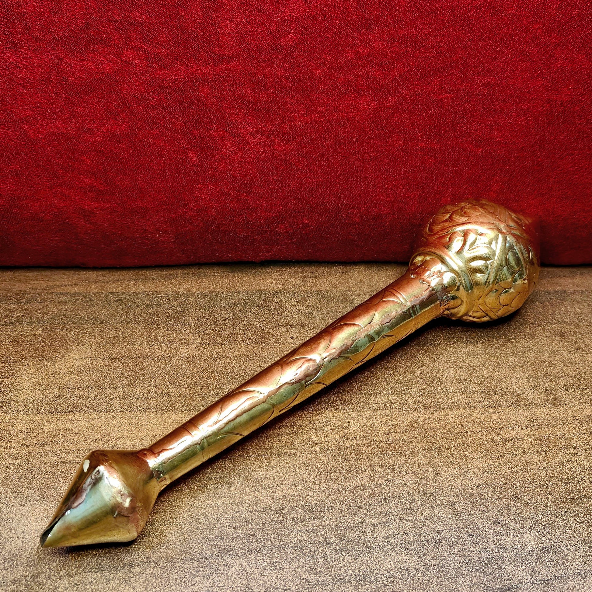 Decorative brass mace on a textured surface with a red background