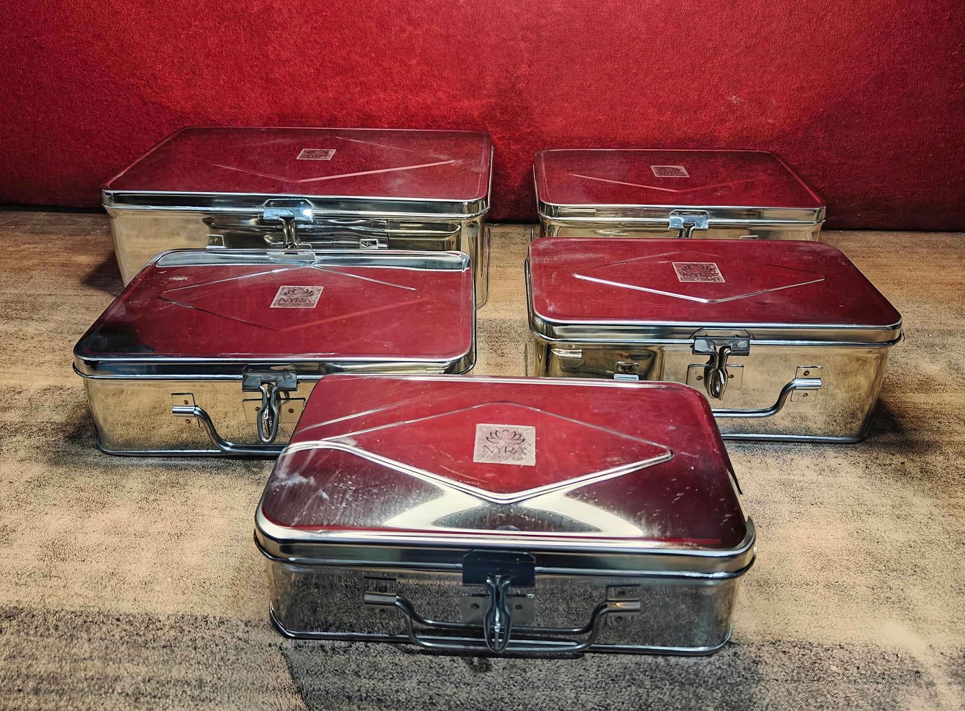 Set of vintage metal suitcases with red and silver finish on a textured surface.