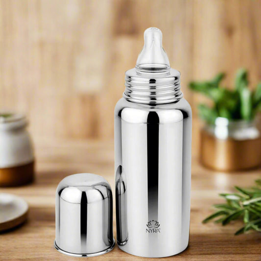 A stainless steel baby feeding bottle with a nipple, alongside its closed cap, presented on a wooden surface.