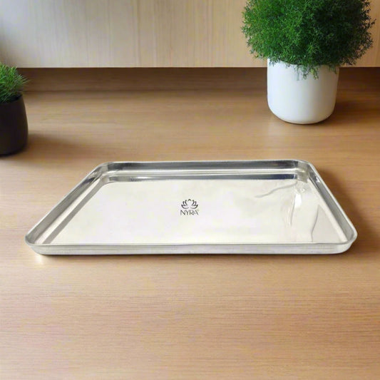A stainless steel serving tray with a glossy finish, placed on a wooden surface, with the Nyra brand logo visible on the tray's edge.
